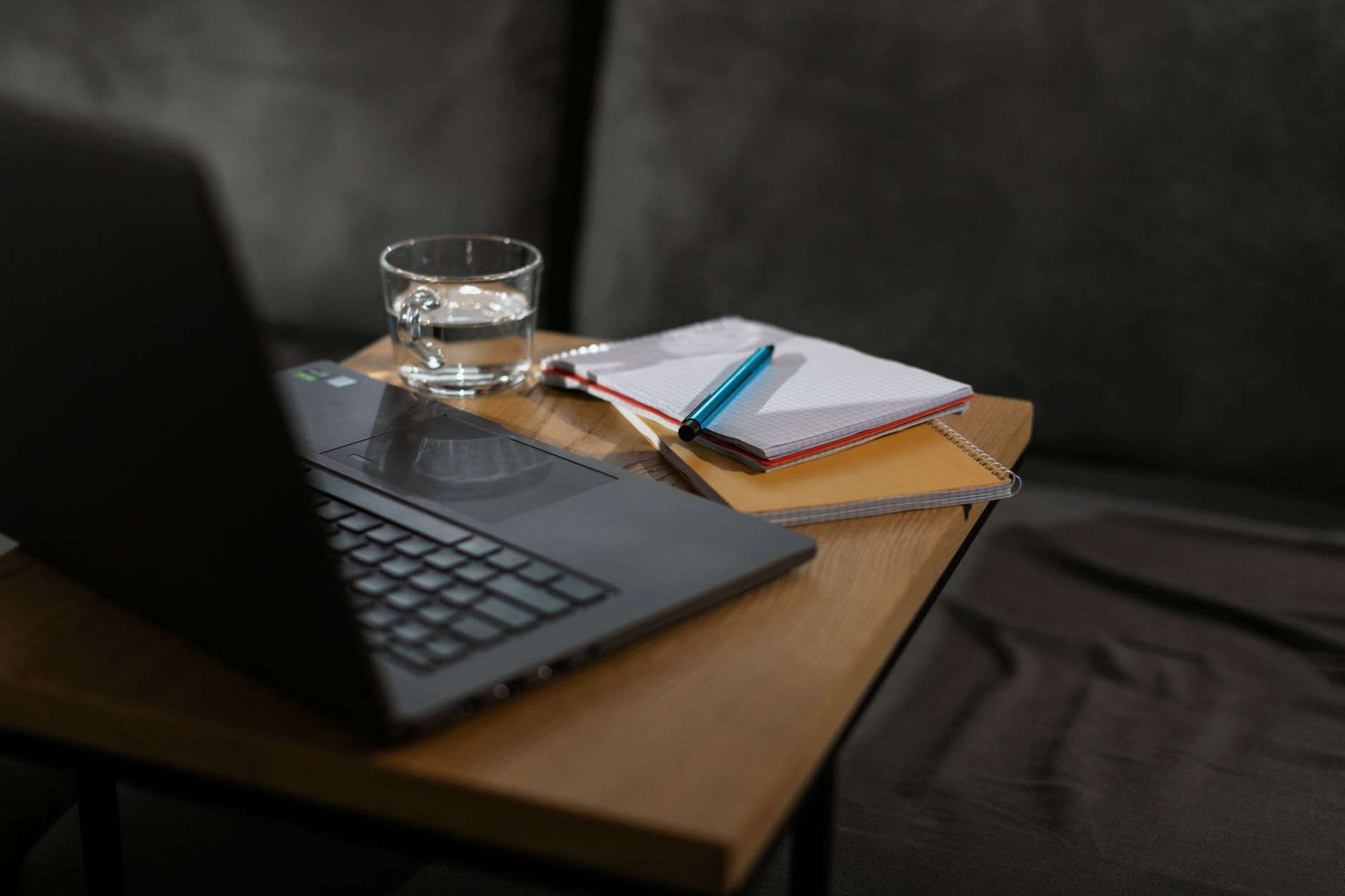 A minimal home desk setup with a laptop, notebook, and a glass of water.