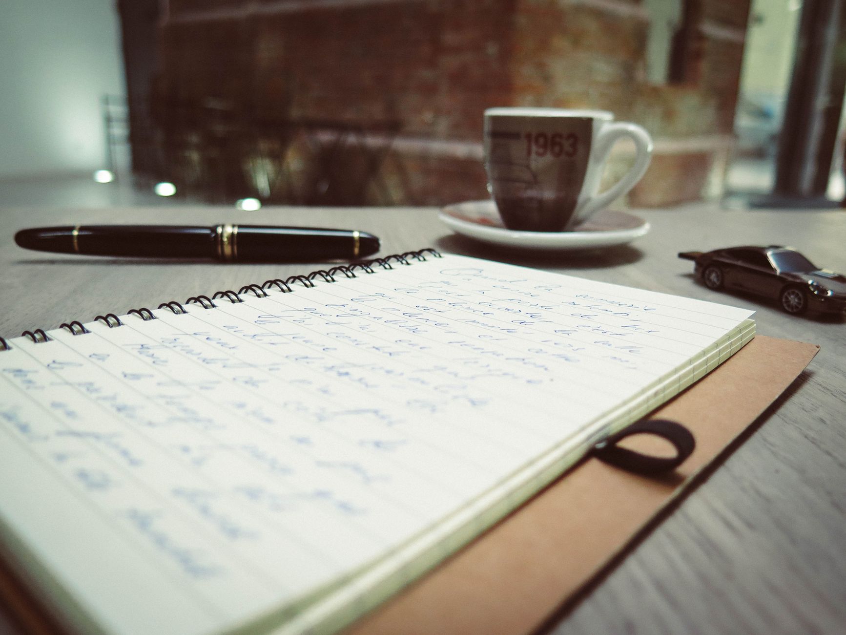 A warm home workspace with coffee, a notebook, and a pen on the desk.